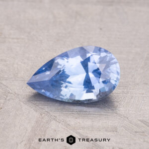 A 1.39-carat Ceylon Sapphire, with a pear-shaped faceted cut, rests on a textured surface labeled "Earth's Treasury.