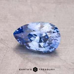 A faceted, pear-shaped blue gemstone named "1.92-Carat Ceylon Sapphire" rests on a textured surface, with “Earth's Treasury” inscribed below.