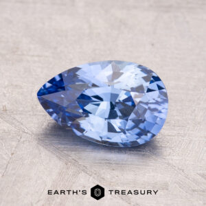 A faceted, pear-shaped blue gemstone named "1.92-Carat Ceylon Sapphire" rests on a textured surface, with “Earth's Treasury” inscribed below.