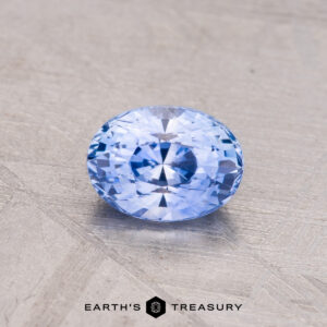 The 1.05-Carat Ceylon Sapphire, a round faceted blue gemstone, rests on a textured surface.