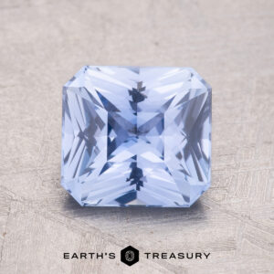 A 2.13-carat Ceylon Sapphire, featuring a light blue square cut and intricate facets, is positioned on a textured surface.