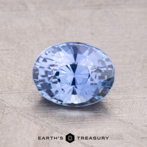 A 1.54-carat Ceylon Sapphire, featuring a round, faceted blue design, is set on a textured surface with the "Earth's Treasury" logo at the bottom.