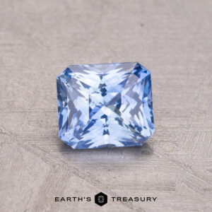 A 1.02-carat square-cut Ceylon Sapphire with intricate facets rests on a textured surface, labeled "Earth's Treasury" below.