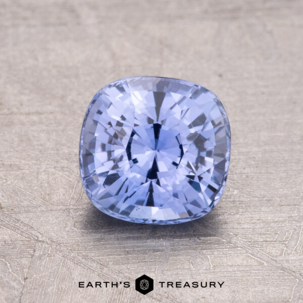 1.55-Carat Ceylon Sapphire A 1.55-carat Ceylon sapphire in a cushion cut sits on a textured surface with the "Earth's Treasury" logo at the bottom.