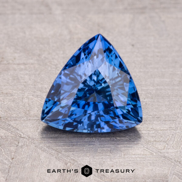 1.52-Carat Ceylon Sapphire A 1.52-carat Ceylon Sapphire, triangular and intricately faceted, rests on a textured surface.