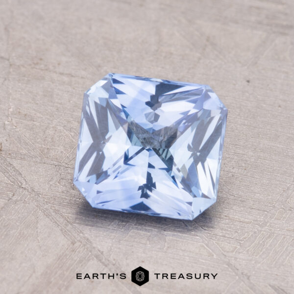1.44-Carat Ceylon Sapphire A 1.44-carat Ceylon Sapphire, square and light blue with intricate faceting, rests on a textured surface, labeled "Earth's Treasury" at the bottom.