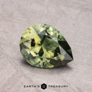 A faceted pear-shaped green gemstone, identified as a 1.49-Carat Australian Sapphire (Heated), rests on a textured gray surface with the "Earth's Treasury" logo and text below.