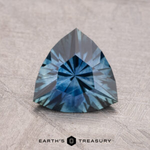 A 1.49-carat heated Montana Sapphire with intricate facets rests against a textured gray background.