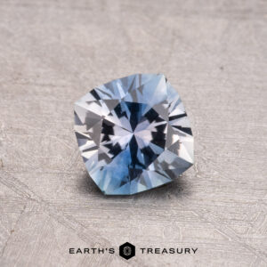 A faceted blue 0.82-carat Montana sapphire (heated) displayed on a textured surface with "Earth's Treasury" below.