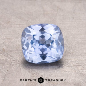 A 1.28-Carat Ceylon Sapphire is displayed on a textured surface featuring the “EARTH’S TREASURY” inscription and a hexagon logo below.
