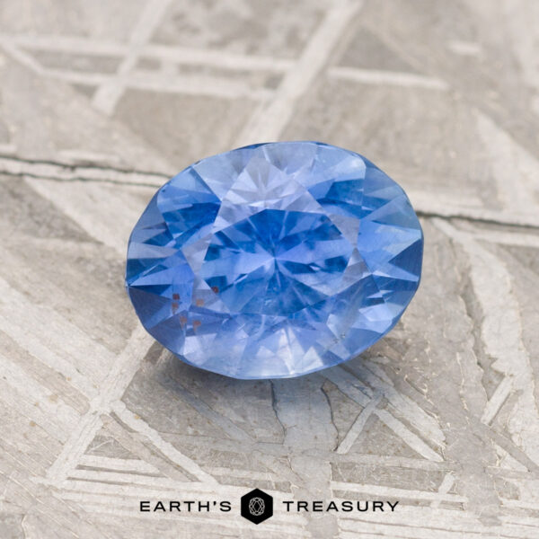 1.85-Carat Cornflower Blue Ceylon Sapphire A 1.85-carat Cornflower Blue Ceylon Sapphire rests on a textured surface, with the "Earth's Treasury" logo at the bottom.
