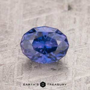 A 1.53-carat purple Ceylon sapphire is showcased on a textured gray surface, exhibiting brilliant reflections.