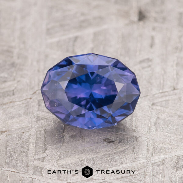 1.53-Carat Purple Ceylon Sapphire A 1.53-carat purple Ceylon sapphire is showcased on a textured gray surface, exhibiting brilliant reflections.