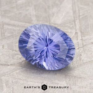 The 1.87-Carat Ceylon Sapphire, an oval stone with a light blue hue, rests on a textured surface, showcasing intricate cuts that beautifully reflect light.