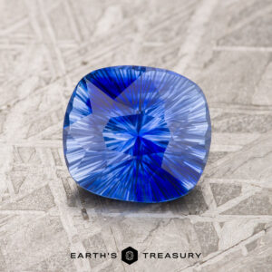 A 3.00-carat rich blue-light blue prticolored Ceylon sapphire with intricate cuts rests on a textured surface, under the "Earth's Treasury" text.