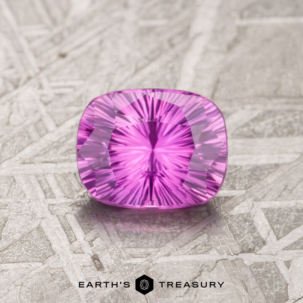 A 1.15-carat hot pink Ceylon sapphire, heated and cushion-cut, rests on a textured surface, exhibiting a symmetrical pattern with a radiant inner glow.