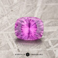 A 1.15-carat hot pink Ceylon sapphire, heated and cushion-cut, rests on a textured surface, exhibiting a symmetrical pattern with a radiant inner glow.