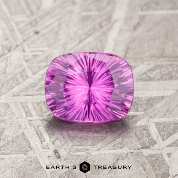 1.15-Carat Hot Pink Celyon Sapphire (Heated) A 1.15-carat hot pink Ceylon sapphire, heated and cushion-cut, rests on a textured surface, exhibiting a symmetrical pattern with a radiant inner glow.