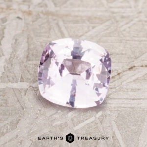 A 1.07-carat light pink Ceylon sapphire cushion-cut gemstone displayed on a textured surface with "Earth's Treasury" beneath.