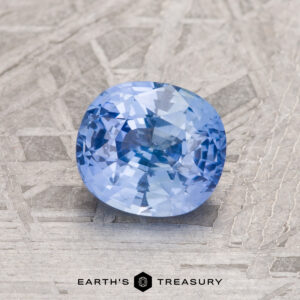 A 1.52-carat Sky Blue Ceylon Sapphire gemstone is showcased on a textured grey surface.