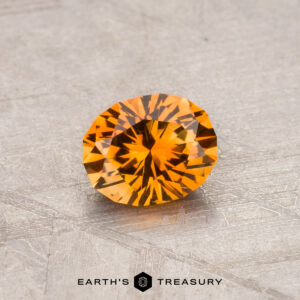 Round, faceted Montana sapphire on a textured surface. Text reads "Earth's Treasury." Product: 0.78-Carat (Heated).