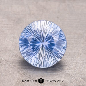 A 2.19-carat Ceylon Sapphire (heated) in a round brilliant cut, displayed on a textured gray surface, with "Earth's Treasury" written below.