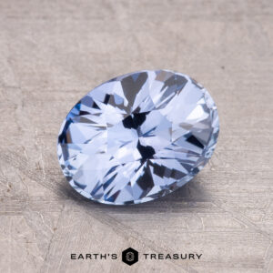 A faceted, oval-cut 2.15-Carat Ceylon Sapphire in light blue displayed on a textured surface with a logo reading "Earth's Treasury" at the bottom.