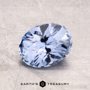 A faceted, oval-cut 2.15-Carat Ceylon Sapphire in light blue displayed on a textured surface with a logo reading "Earth's Treasury" at the bottom.