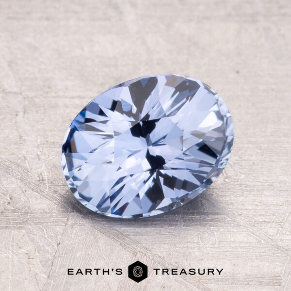2.15-Carat Ceylon Sapphire A faceted, oval-cut 2.15-Carat Ceylon Sapphire in light blue displayed on a textured surface with a logo reading "Earth's Treasury" at the bottom.