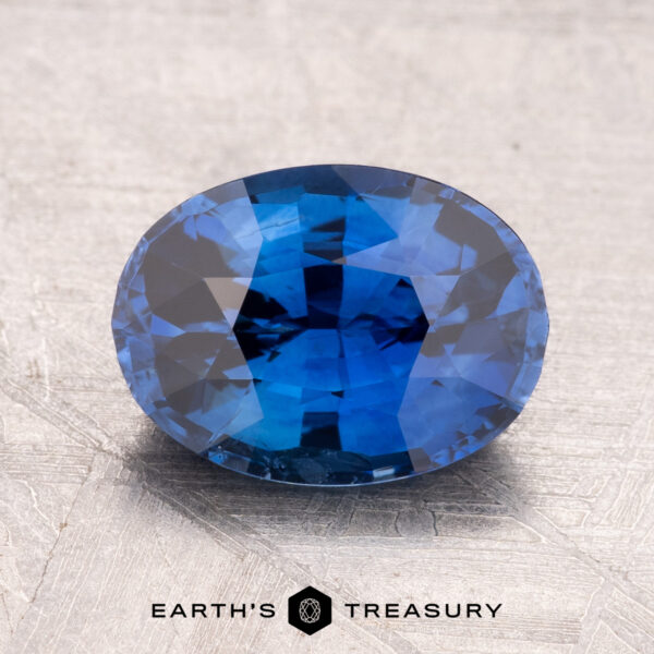 2.44-Carat Ceylon Sapphire (Heated) A 2.44-carat heated Ceylon sapphire, faceted in an oval shape, rests on a textured gray surface. Text reads "Earth's Treasury.