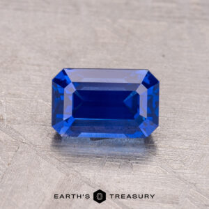 A 1.48-carat Ceylon sapphire (heated) in a rectangular shape on a textured gray background with "Earth's Treasury" at the bottom.