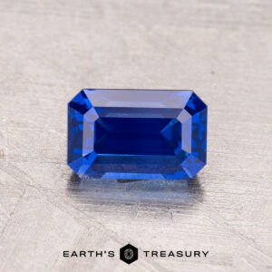 A 1.48-carat Ceylon sapphire (heated) in a rectangular shape on a textured gray background with "Earth's Treasury" at the bottom.