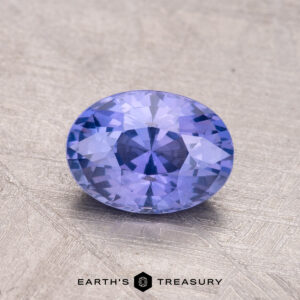 An oval-cut, faceted Ceylon Sapphire (1.32 carats) lies on a textured surface with the "Earth's Treasury" logo below.