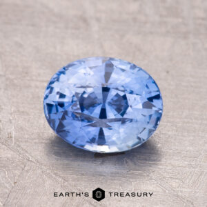A faceted blue gemstone, the 2.07-Carat Ceylon Sapphire, is presented on a textured surface with the "Earth's Treasury" logo below.