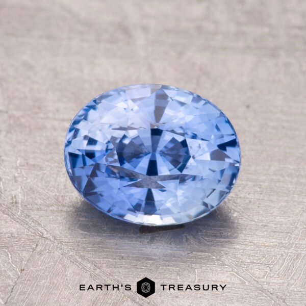2.07-Carat Ceylon Sapphire A faceted blue gemstone, the 2.07-Carat Ceylon Sapphire, is presented on a textured surface with the "Earth's Treasury" logo below.