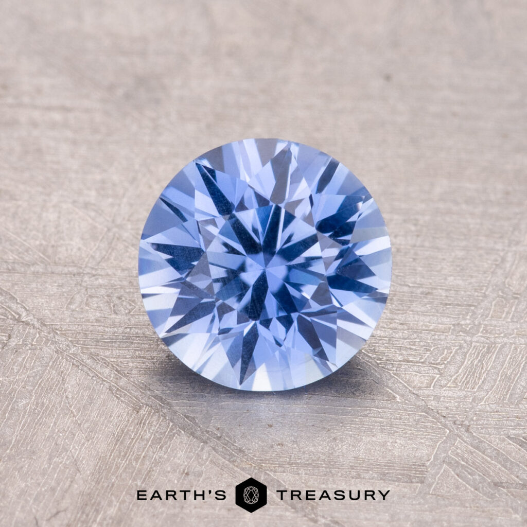 A 1.16-carat Ceylon Sapphire with a round facet rests on a textured beige surface.