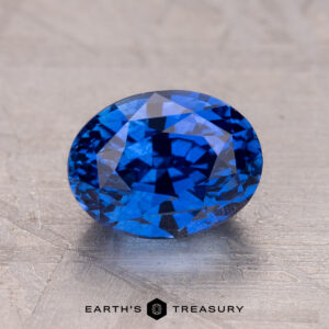A 2.53-carat Ceylon sapphire with a faceted cut rests on a textured gray surface.