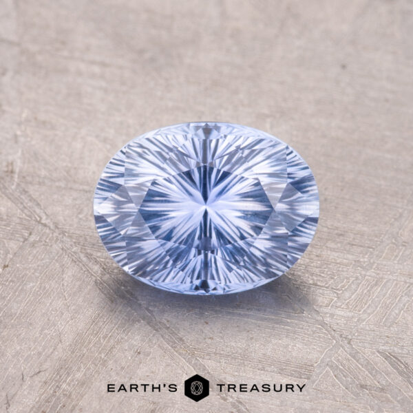 1.47-Carat Ceylon Sapphire A faceted, oval-cut blue gemstone, the 1.47-Carat Ceylon Sapphire, rests on a textured surface with "Earth's Treasury" text visible at the bottom.