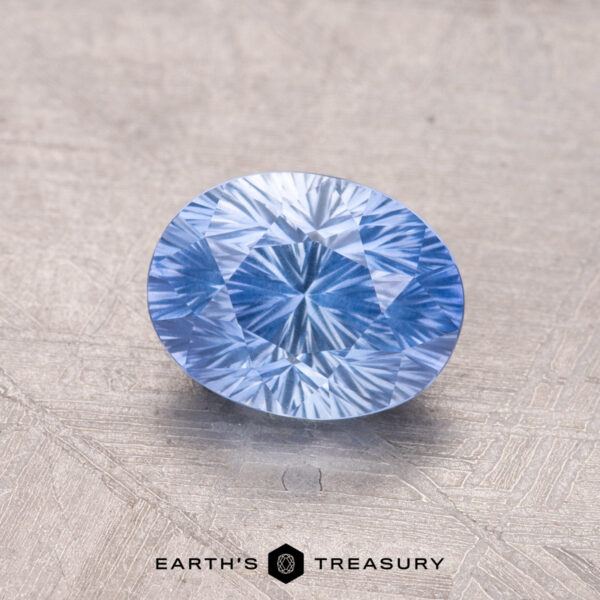 1.34-Carat Ceylon Sapphire A blue oval-cut 1.34-carat Ceylon Sapphire gemstone is displayed on a textured surface with "Earth's Treasury" text at the bottom.