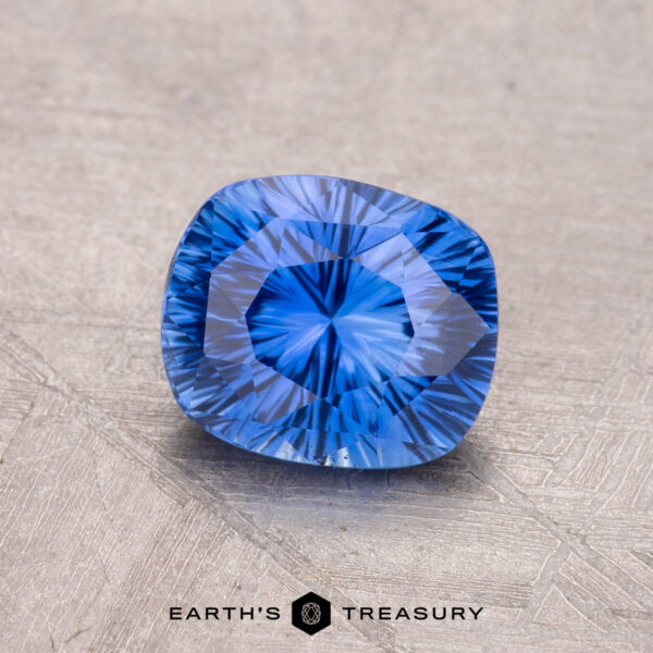 1.45-Carat Ceylon Sapphire A vibrant blue 1.45-Carat Ceylon Sapphire with intricate facets lies on a textured surface, with "Earth's Treasury" visible below.