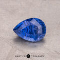 A teardrop-shaped 1.38-Carat Ceylon Sapphire rests on a textured surface, with "Earth's Treasury" visible at the bottom.