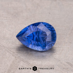 A teardrop-shaped 1.38-Carat Ceylon Sapphire rests on a textured surface, with "Earth's Treasury" visible at the bottom.