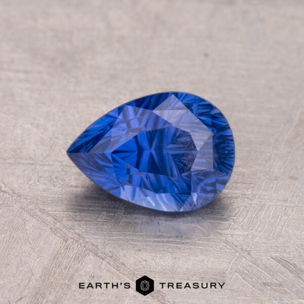 1.38-Carat Ceylon Sapphire A teardrop-shaped 1.38-Carat Ceylon Sapphire rests on a textured surface, with "Earth's Treasury" visible at the bottom.
