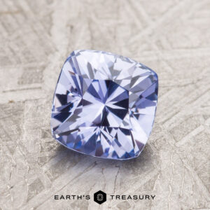 A 1.60-carat light violet Ceylon sapphire on a textured surface, labeled "Earth's Treasury.