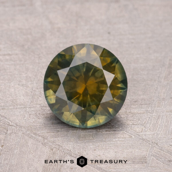 1.33-Carat Montana Sapphire (Heated), a round green gemstone with yellow tones on a textured surface, features the "Earth's Treasury" logo below it.