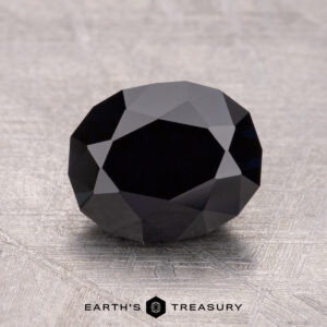 A 2.33-carat near-black Australian sapphire (heated) is intricately faceted and rests on a textured surface.