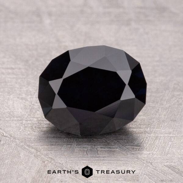 2.33-Carat Australian Sapphire (Heated) A 2.33-carat near-black Australian sapphire (heated) is intricately faceted and rests on a textured surface.
