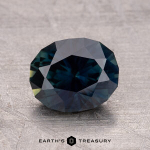A 2.29-carat round-cut Australian sapphire in dark blue appears on a textured surface, with "Earth's Treasury" beneath it.