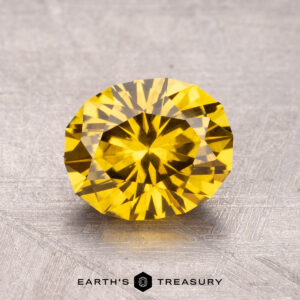 A 1.96-carat Australian sapphire (heated) with a round, faceted cut rests on a textured gray surface.