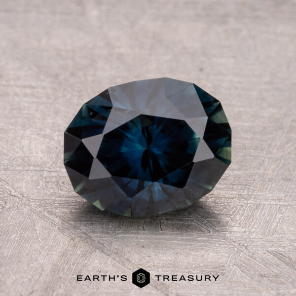 1.85-Carat Australian Sapphire (Heated) A 1.85-carat Australian sapphire (heated) in dark blue with facets lies on a textured light gray surface, labeled "Earth's Treasury.